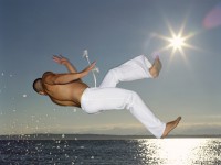 Young man performing capoeira on beach at dusk